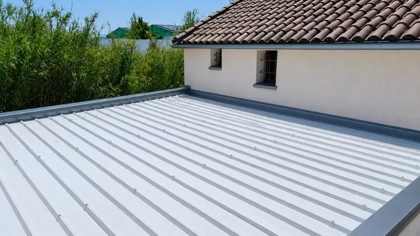 Couverture en bac acier clair sur une extension, avec ses bandes de rive et son relevé contre le mur de la maison