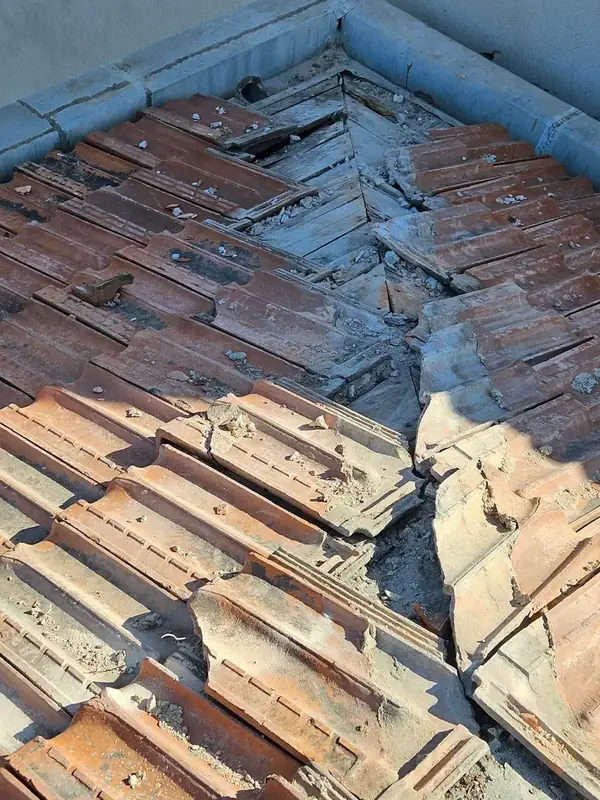 Tuiles anciennes cassées et mortier effrité autour d’une noue, voliges en bois visibles au fond